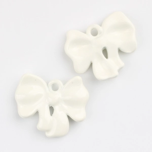 Detail of two cream white alloy bow pendants with glossy enamel finish for DIY jewelry