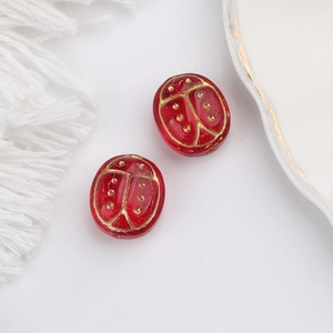 Macro detail of red Czech glass ladybug beads with gold-painted accents for DIY jewelry