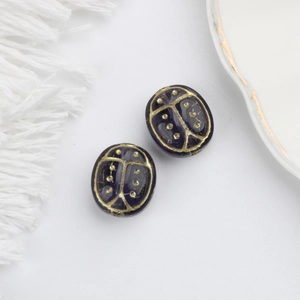 Macro detail of purple Czech glass ladybug beads with gold hand-painted accents for DIY jewelry