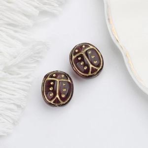 Close-up of dark red Czech glass beads with gold ladybug engraving for jewelry DIY