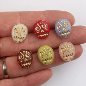 Handheld display of six colorful Czech glass skull beads with detailed gold engraving