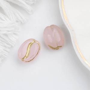 Macro shot of oval vintage glass beads in translucent pink with gold floral patterns