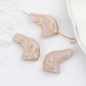 Vista macro di perle in vetro rosa a forma di cane con bordi dorati per gioielli DIY