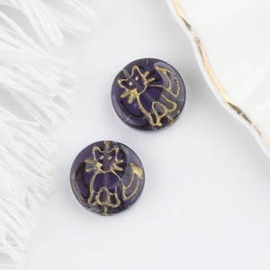 Macro view of purple Czech glass beads with double-sided gold cat motif for DIY