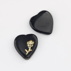 Macro shot of two heart-shaped black glass beads with golden floral relief for DIY jewelry