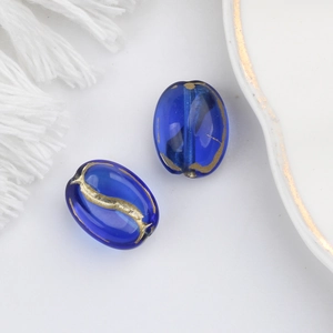 Detailed view of deep blue oval coffee bean glass beads with gold painted texture for DIY