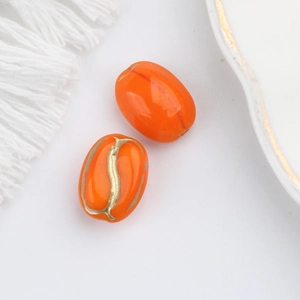 Detailed macro view of orange oval glass beads with gold painted coffee bean texture