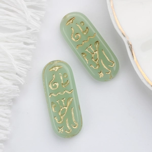 Detailed view of light green Czech glass beads with golden Egyptian rune engravings