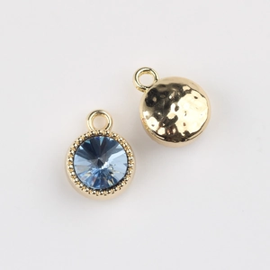 Detail view of round gold-plated pendant with blue crystal and hammered metal back
