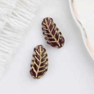 Detailed view of dark red Czech glass leaf beads with gold vein texture for jewelry