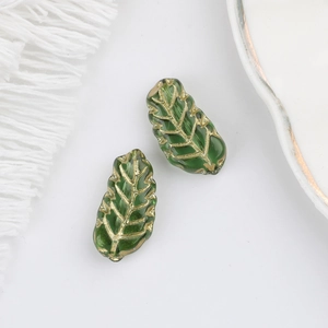 Macro detail of green glass leaf beads with gold vein textures on a white surface