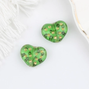 Dettaglio di perline di vetro verde a forma di cuore con pois dorati per gioielli
