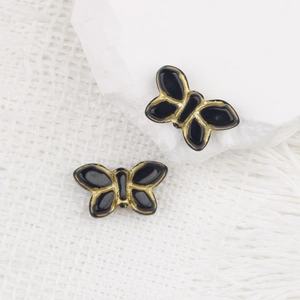Dettaglio macro di perle a farfalla ceche vintage con smalto nero e finiture in oro