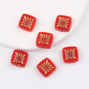 Macro view of six red square Czech glass beads with gold starburst patterns for jewelry