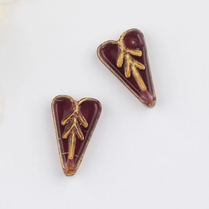 Detailed view of burgundy Czech glass heart beads with vintage gold leaf pattern for DIY jewelry