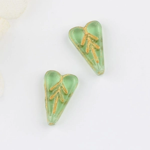 Macro detail of heart-shaped green glass beads with hand-painted gold leaf patterns