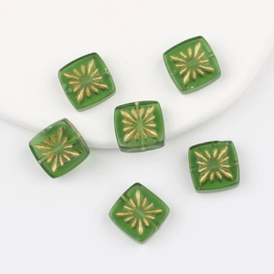Macro detail of 10mm green square glass beads with golden hand-painted firework patterns