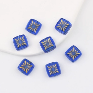 Macro view of blue square glass beads with hand-painted gold sunburst floral designs
