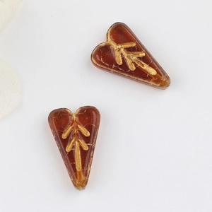 Macro detail of amber Czech glass heart beads with vintage gold leaf patterns for DIY jewelry