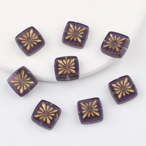 Macro view of purple square glass beads with hand-painted gold starburst patterns for DIY