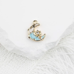 Détail d'un pendentif lune en émail bleu avec rose dorée et zircon sur fond blanc