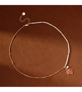 Détail d'un collier pendentif feuille d'érable rouge et perles sur velours marron