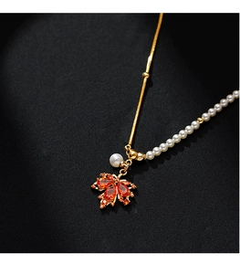 Détail macro du pendentif feuille d'érable rouge avec perle asymétrique et chaîne dorée