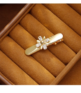 Détail d'une barrette fleur dorée en zircon posée sur un présentoir en velours marron