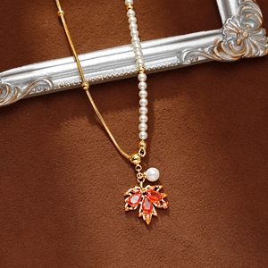 Collier feuille d'érable asymétrique avec zircons rouges et perles sur texture automne
