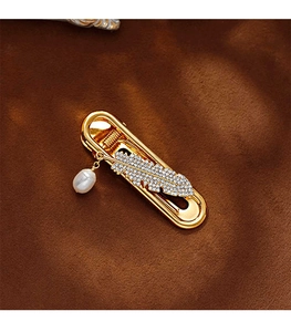 Detail of gold metal hair clip with rhinestone feather and baroque pearl on brown suede