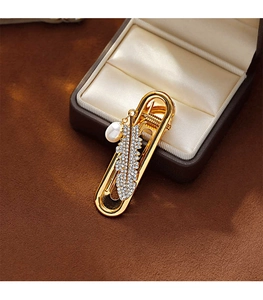 Detailed close-up of a golden U-shaped hair clip with a diamond feather and white pearl
