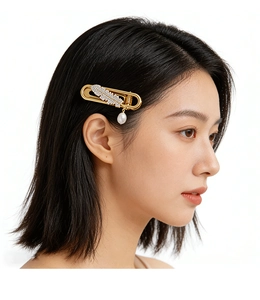 Detail of a gold feather hair clip with sparkling rhinestones and a white freshwater pearl