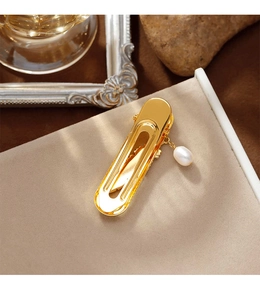 Detailed view of a gold hair clip with freshwater pearl pendant on a beige texture
