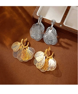Detailed view of layered gold and silver tassel leaf clip-on earrings on wooden box