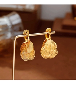 Detailed view of golden leaf tassel earrings with brushed metal texture and clip-on design