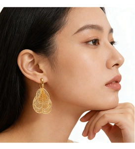 Close-up of golden hollow fan-shaped leaf earrings worn by a model in soft lighting