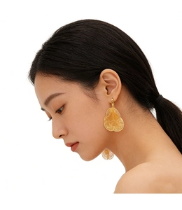 Close-up of gold leaf-shaped filigree earrings worn by a model in a side view