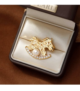Détail de la broche cheval à bascule doré avec perle et zircons dans un coffret cadeau