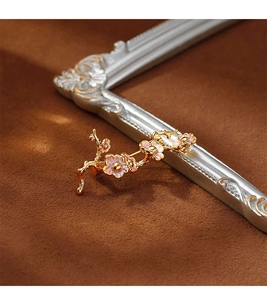 Détail macro d'une broche branche dorée avec pétales en émail rose sur velours marron