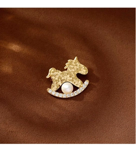 Détail de la broche cheval à bascule doré avec perle blanche et zircons brillants
