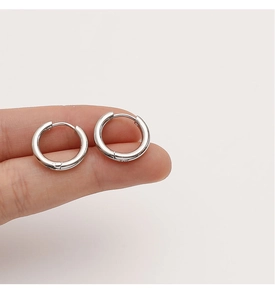 Gros plan de petites créoles huggie en argent poli tenues entre les doigts