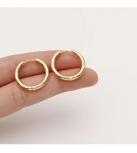 Vue détaillée de petites boucles d'oreilles huggie dorées polies sur le bout des doigts