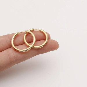 Boucles d'oreilles créoles dorées minimalistes avec finition polie tenues par les doigts