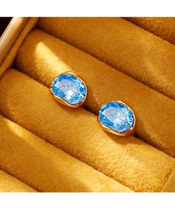 Detailed view of oval blue zircon earrings with gold wavy frames in a velvet box