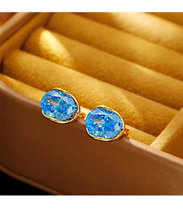Macro shot of oval blue zircon earrings with a gold metal base on a velvet jewelry box