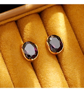 Macro shot of oval purple zircon earrings with gold wavy frames in a velvet box