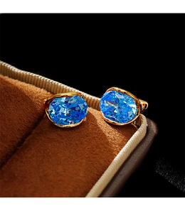Macro shot of oval blue zircon earrings set in gold metal on a velvet box