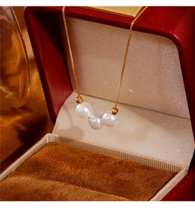 Macro de tres perlas blancas y cuentas doradas en una cadena en O en una caja de regalo