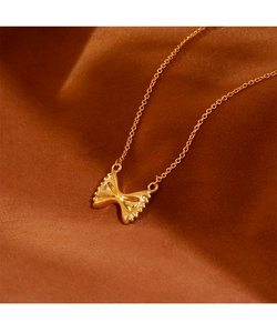 Detail van een gepolijste gouden strik hanger aan een fijne ketting op bruine zijde