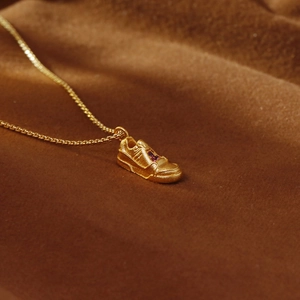 Collana con ciondolo a scarpa dorata e gemma viola su velluto marrone scuro